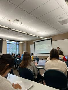 people are sitting at tables in front of laptops and projector screens as they watch a presentation