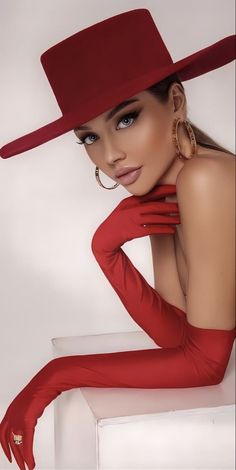 a woman in a red dress and hat posing for the camera with her hands on her hips