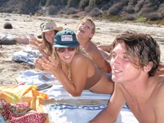 four people are laying on the beach with towels around them and one person is wearing a hat