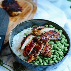 a bowl filled with meat and green beans next to a knife on top of a cutting board