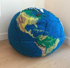 a large blue knitted globe sitting on top of a wooden floor next to a white wall