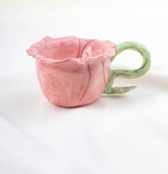 two ceramic cups sitting next to each other on a white tableclothed surface, one is pink and the other has green handles