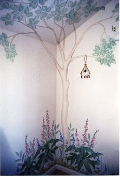 a tree painted on the side of a wall next to a potted plant and bird feeder