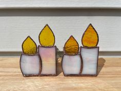 three stained glass candles sitting next to each other on a wooden table with a white door in the background