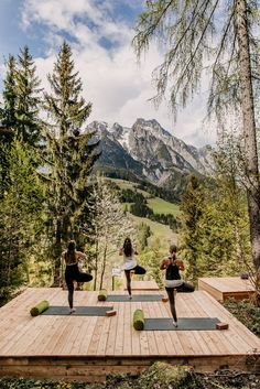 three women are doing yoga on a wooden platform with mountains in the backgroud