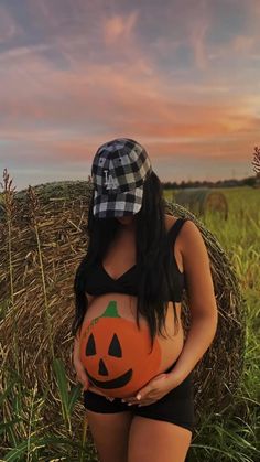 a pregnant woman holding a pumpkin in her belly while wearing a black and white checkered hat