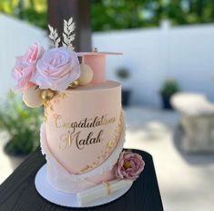 a pink and gold wedding cake with flowers on top is sitting on a table outside