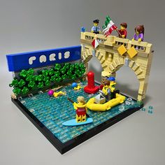 a lego model of people on a boat in the water near a bridge and trees