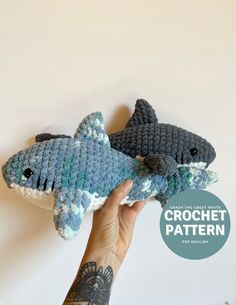 two crocheted stuffed sharks are being held up by a person's hand