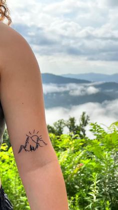 a woman with a tattoo on her arm looking out at the mountains and clouds in the distance