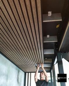 a man is working on the underside of a wooden ceiling in an office building with windows