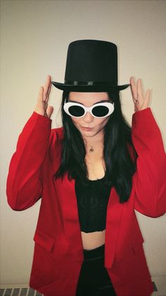 a woman in a red jacket and black top hat with sunglasses on her head wearing a fedora