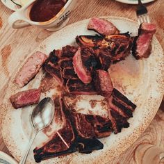 a white plate topped with sliced up meat next to a fork and bowl filled with sauce