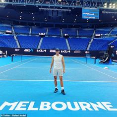 a man standing on top of a tennis court in front of an empty stadium filled with blue seats