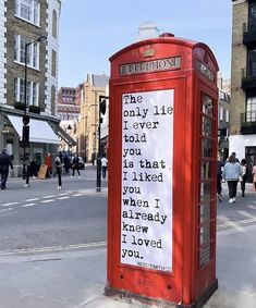 a red phone booth sitting on the side of a road next to people walking around