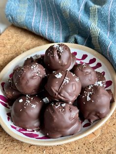 a bowl filled with chocolate covered donuts on top of a wooden table next to a blue towel