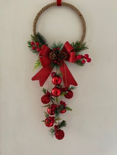 a wreath with pine cones and red ornaments hanging on a wall