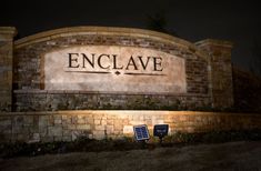 the entrance sign to enclave at night with two solar powered lights on it's sides