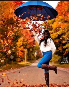 a woman holding an umbrella over her head while standing in the middle of autumn leaves