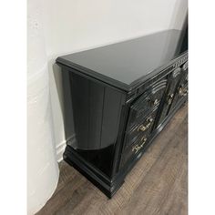 a black cabinet sitting on top of a hard wood floor next to a white wall