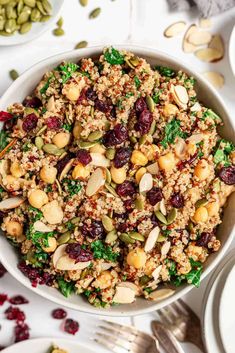 a white bowl filled with nuts, cranberries and quinoa salad next to silverware