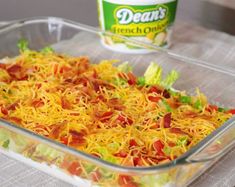 a glass casserole dish filled with shredded cheese and veggies next to a can of dean's dressing