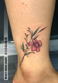 a small flower tattoo on the side of a woman's foot with green leaves