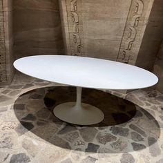 an oval white table sitting on top of a stone floor next to a brick wall