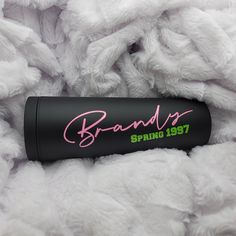 a black tube with pink writing sitting on top of a pile of fluffy white blankets