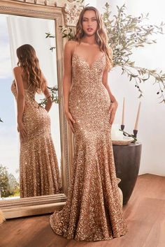 a woman standing in front of a mirror wearing a gold sequinned evening gown