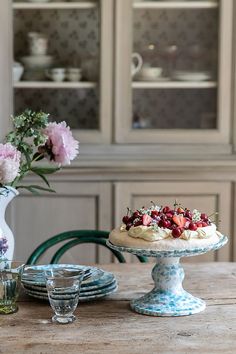 a table topped with a cake covered in strawberries next to vases filled with flowers