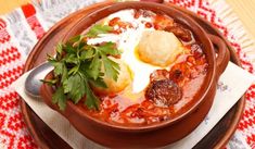 a bowl filled with meat and vegetables on top of a red table cloth next to a spoon