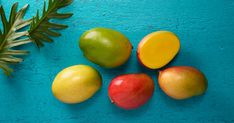 four different types of fruit on a blue surface next to a green plant and leaf