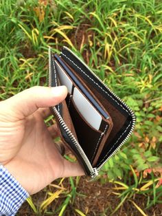 someone is holding their wallet open in front of some grass and plants with one hand