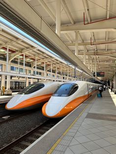 two orange and white trains parked at a train station