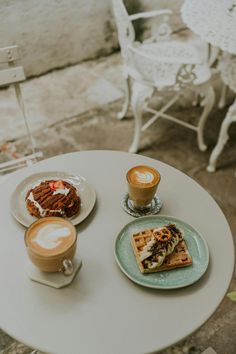 two plates with waffles, coffee and other food on them sitting on a table