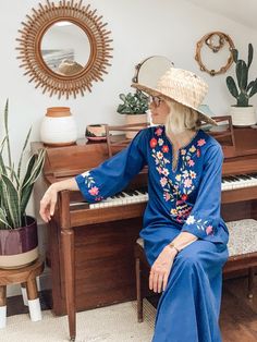 a woman sitting on top of a wooden piano in front of a potted plant