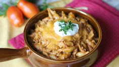 a close up of a bowl of chili macaroni and cheese with tomatoes in the background