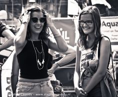 two young women standing next to each other in front of a crowd with sunglasses on