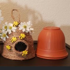 two small baskets with flowers are on a table next to an orange vase and cone