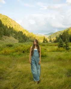 a woman standing in the middle of a field with mountains in the backgroud