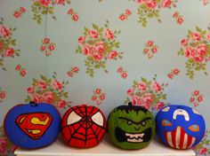 three painted pumpkins with different designs on them sitting on a shelf in front of a floral wallpaper