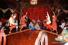 some people are dancing on a wooden floor with red curtains and drapes behind them