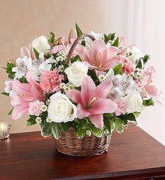 a basket filled with pink and white flowers sitting on top of a table next to a lit candle