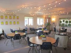 an empty room with tables and chairs, lights strung from the ceiling and posters on the wall