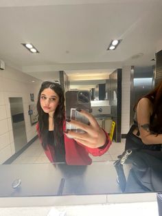 a woman taking a selfie with her cell phone in a public restroom stall area