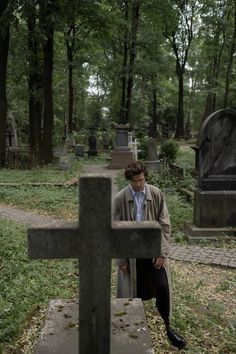 a man sitting on top of a wooden cross in a cemetery next to a grave