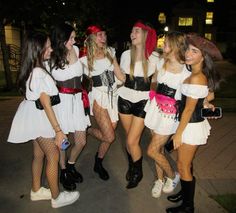 four girls dressed up in costumes standing on the street at night with one girl holding her cell phone