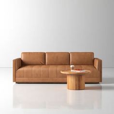 a brown leather couch sitting next to a wooden table on top of a white floor