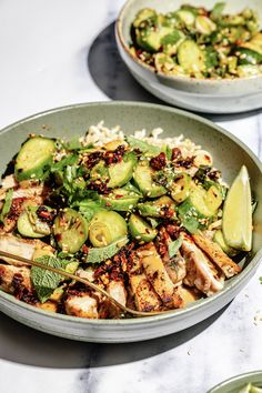 two bowls filled with chicken, cucumbers and rice on top of a table